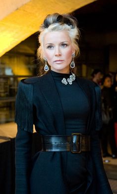 a woman standing in front of a crowd wearing a black dress and statement necklaces