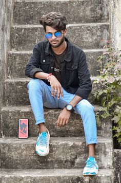 a man sitting on the steps with his feet up and wearing blue jeans, a black shirt and white sneakers