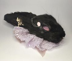 a black rat with pink eyes wearing a white lace garter and chain around its neck