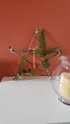 a candle is sitting on a table next to a glass bowl with pine branches in it