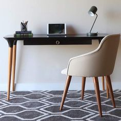 a desk with two chairs and a laptop computer on it, in front of a white wall