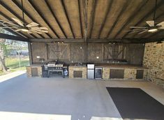 an outdoor kitchen area with stone walls and ceiling fans, grilling tables and refrigerators