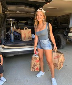 a woman holding two bags standing in front of a car