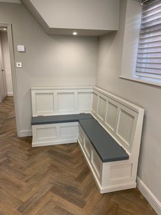 an empty room with white paneling and wood flooring on the walls, along with a gray bench