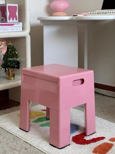 a pink stool sitting on top of a white rug in front of a book shelf