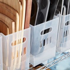 plastic storage bins with wooden utensils and cutting boards in them on a metal rack