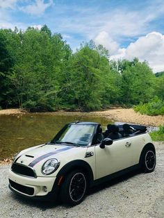 a small white car parked on top of a gravel road next to a river and forest