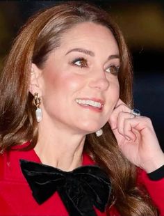 a woman wearing a red coat and black bow tie with her hand on her chin