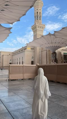 a person in a white robe walking under an umbrella covered walkway near a large building