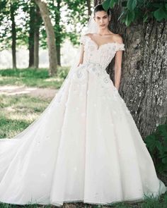 a woman standing next to a tree wearing a wedding dress with flowers on the skirt