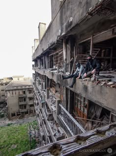 two men sitting on the ledge of an old building in ruins, one is holding his leg up