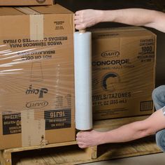 a man is holding a roll of white paper in front of cardboard boxes on a pallet