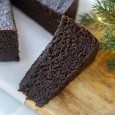 chocolate cake sitting on top of a wooden cutting board next to a pine tree with one slice cut out