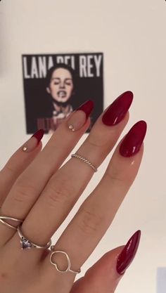 a woman's hand with red manies and rings on it, in front of a poster