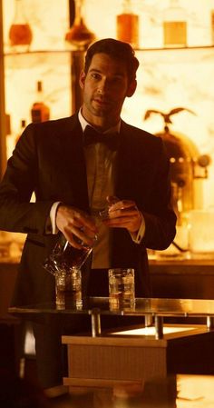 a man in a tuxedo standing at a table with two glasses on it