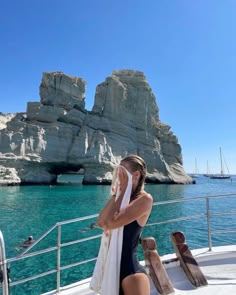 a woman standing on the deck of a boat in front of some rocks and water