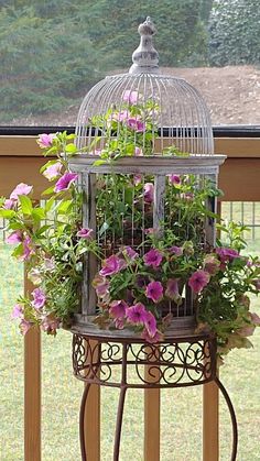 a birdcage filled with flowers sitting on top of a wooden deck next to a fence