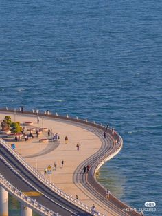 an aerial view of the ocean with people walking on it and cars driving down the road