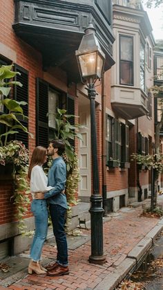 a man and woman standing next to each other in front of a lamp post on a city street