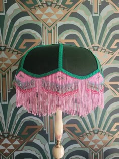 a green and pink lamp with fringes on it in front of a wallpapered background