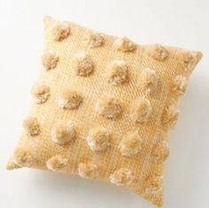 a yellow and white pillow with pom - poms on the front, sitting on a white surface