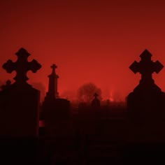 two crosses are silhouetted against the red sky at sunset in an old cemetery graveyard