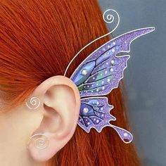 a close up of a person with red hair wearing a butterfly earring and piercings