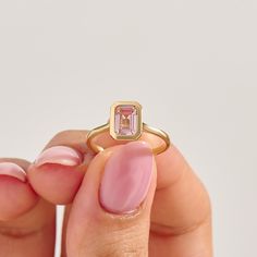 a woman's hand holding a ring with a pink stone