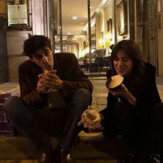 two people sitting on the ground eating food and drinking from cups in front of them