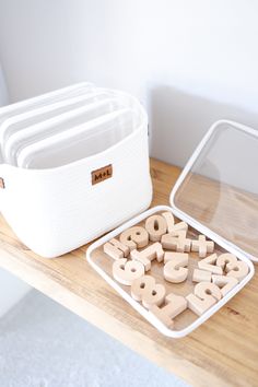 wooden letters and numbers sit on a table next to a container with plastic containers in it