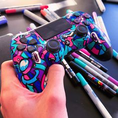 a person holding a video game controller in front of markers and pens on a table