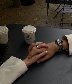 two people holding hands with coffee cups in the background