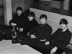 black and white photograph of four men sitting on the floor in an office setting with one man holding his leg up