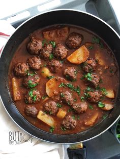 a pan filled with meatballs and potatoes on top of a stove next to a napkin