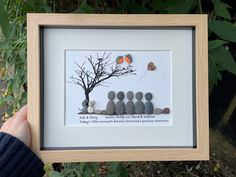 a person holding up a framed photo with rocks in the shape of a tree and butterflies