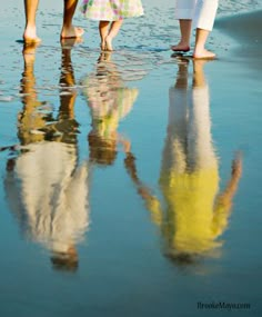 three people standing on the beach with their feet in the water and one person walking behind them