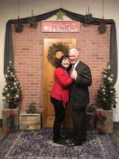 a man and woman standing in front of a brick wall with christmas wreaths on it