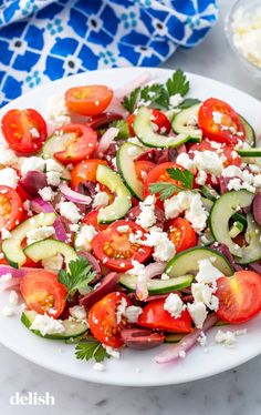 a white plate topped with cucumber, tomatoes and feta cheese on top of a table