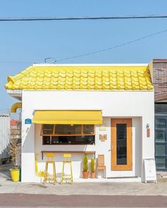 a small white building with yellow awnings on the roof and two stools outside