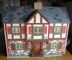 a doll house made out of paper on top of a wooden table next to a window