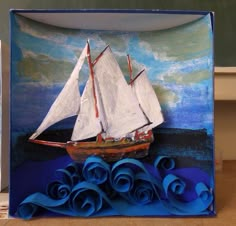 a paper sculpture with a sailboat on the water and blue waves in front of it