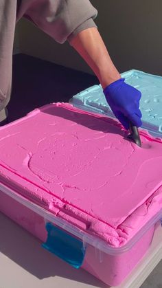 a person in blue gloves is decorating a cake with pink icing on it