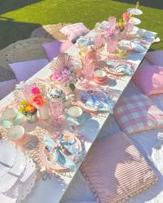 a table set with plates, cups and saucers on top of a blanket in the grass