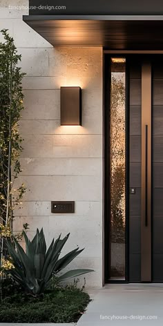 the front door to a modern home is lit up by two wall lights and plants