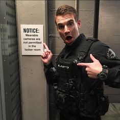 a man in a police uniform points at a sign that reads notice cameras are not permitted in the locker room