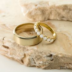 two gold wedding rings sitting on top of a rock next to another ring with diamonds