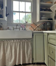 a kitchen with green cabinets and white counter tops, along with a window over the sink