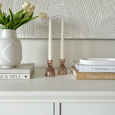 three candles are sitting on a white dresser next to some books and a vase with tulips in it