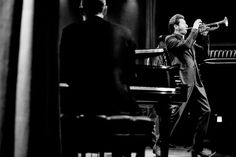 a man in a suit and tie playing a trumpet next to another man sitting at a piano