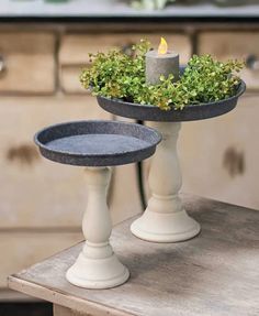 two candles are sitting on top of a tray with some plants in it and one candle is lit